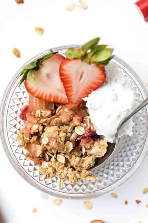 Strawberry rhubarb crisp in bowl with scoop of coconut cream