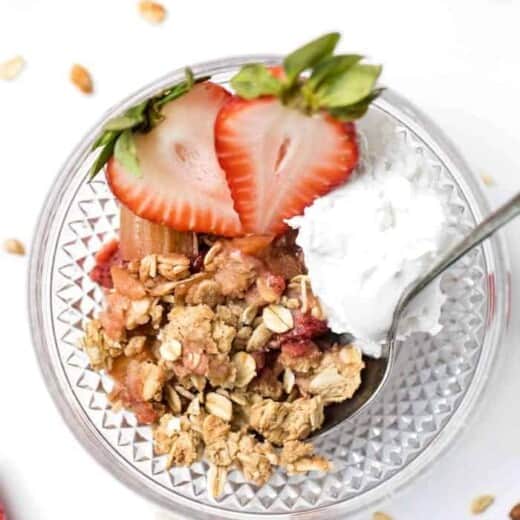 Strawberry rhubarb crisp in bowl with scoop of coconut cream