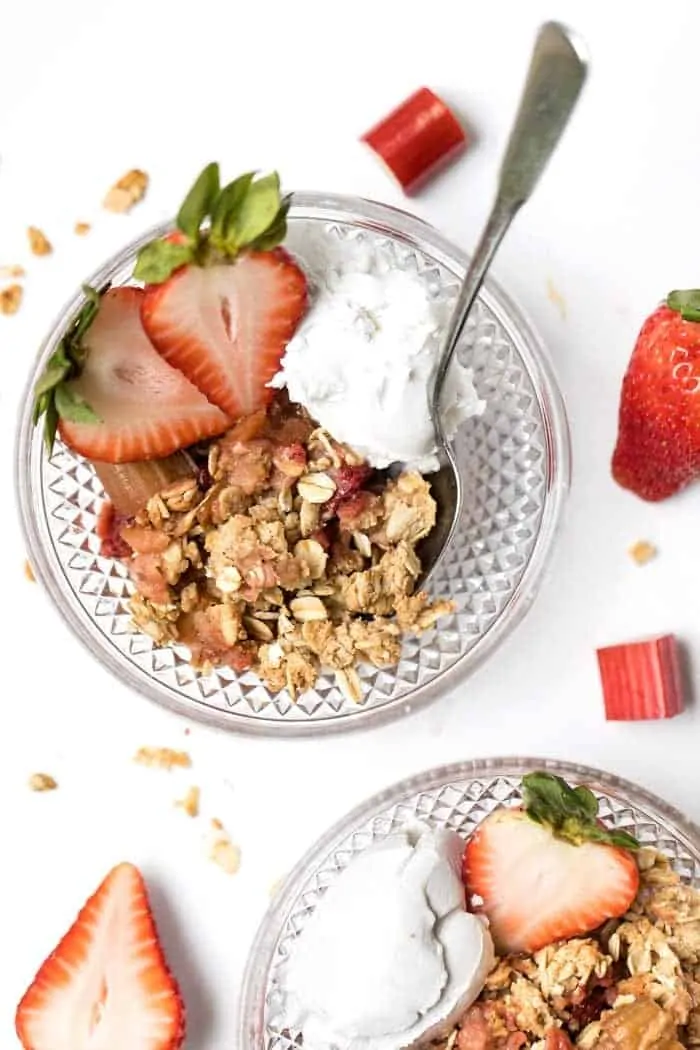 Overhead view of strawberry rhubarb crisp in bowls with coconut cream and fresh berries for garnish