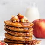 Stack of fluffy oatmeal pancakes topped with apples and pecans