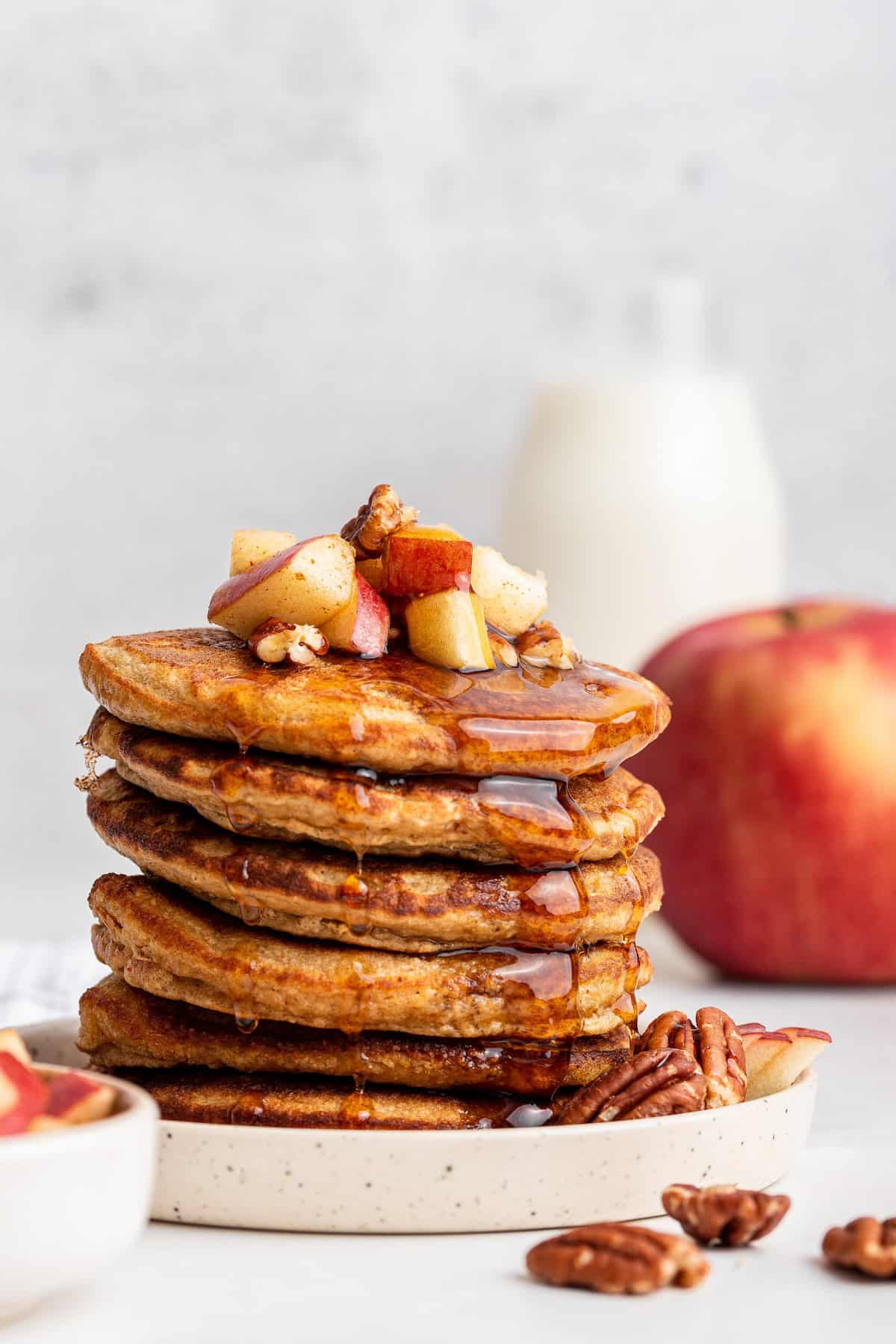 Stack of fluffy oatmeal pancakes topped with apples and pecans