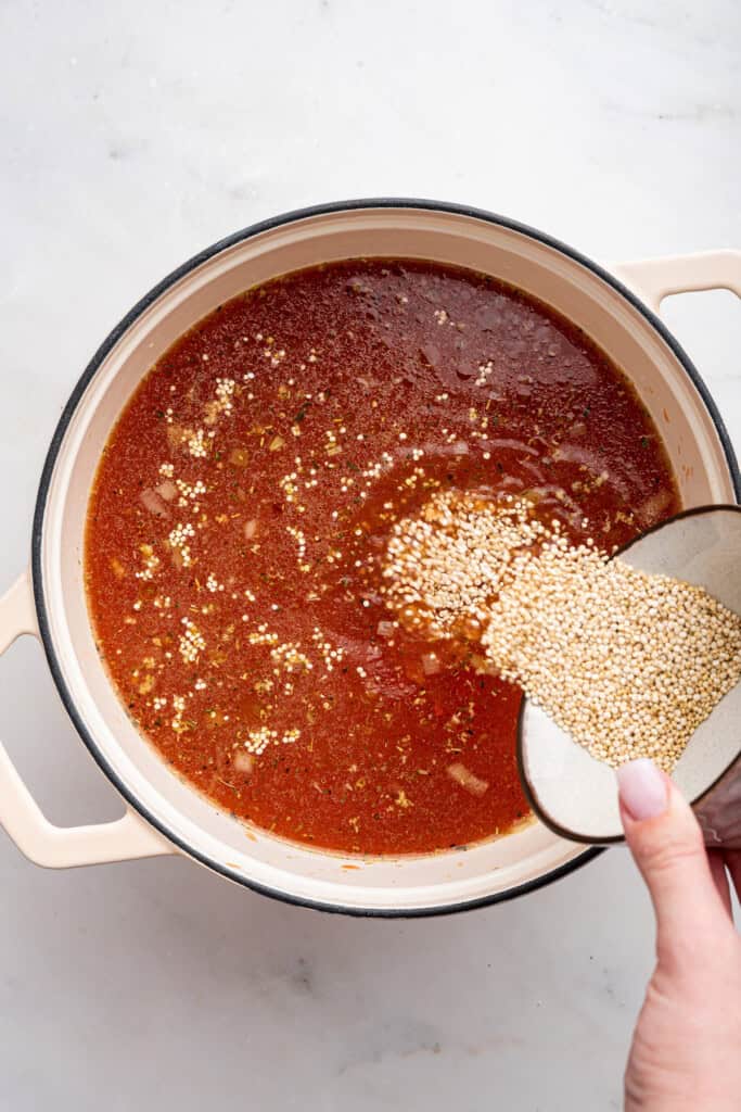 Adding quinoa to a pot with tomato bisque.