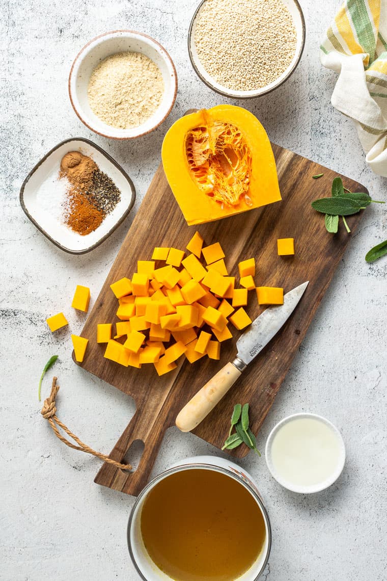 Overhead view of chopped butternut squash next to one half of a butternut squash on a cutting board.