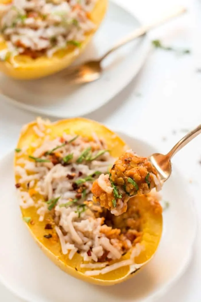 A forkful held over a spaghetti squash boat on a white plate, with a second squash boat on a plate in the background.