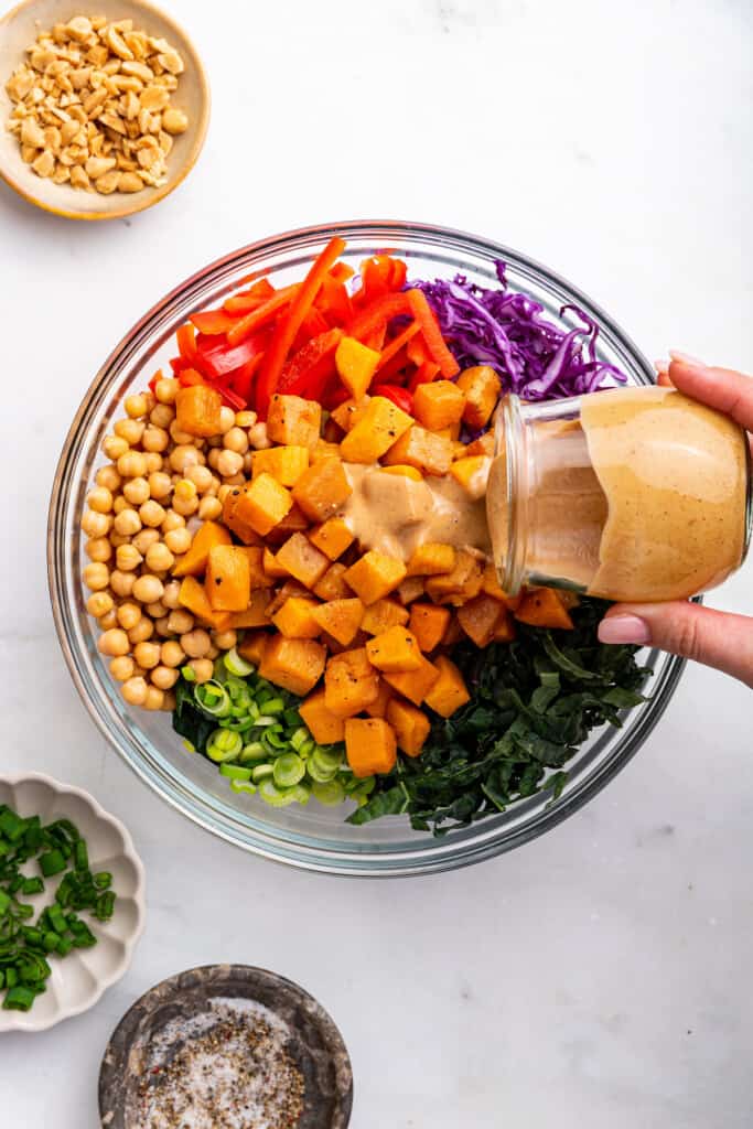 Pouring Thai almond dressing into bowl of salad ingredients