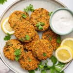 Overhead view of lentil patties on plate with cup of sauce and lemon slices