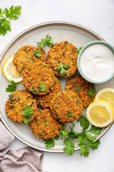 Overhead view of lentil patties on plate with cup of sauce and lemon slices