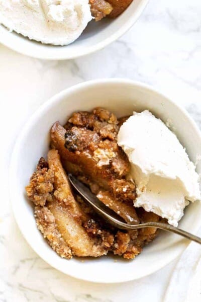 Overhead view of a bowl of gluten-free apple crisp topped with a scoop of vegan ice cream, with a spoon.