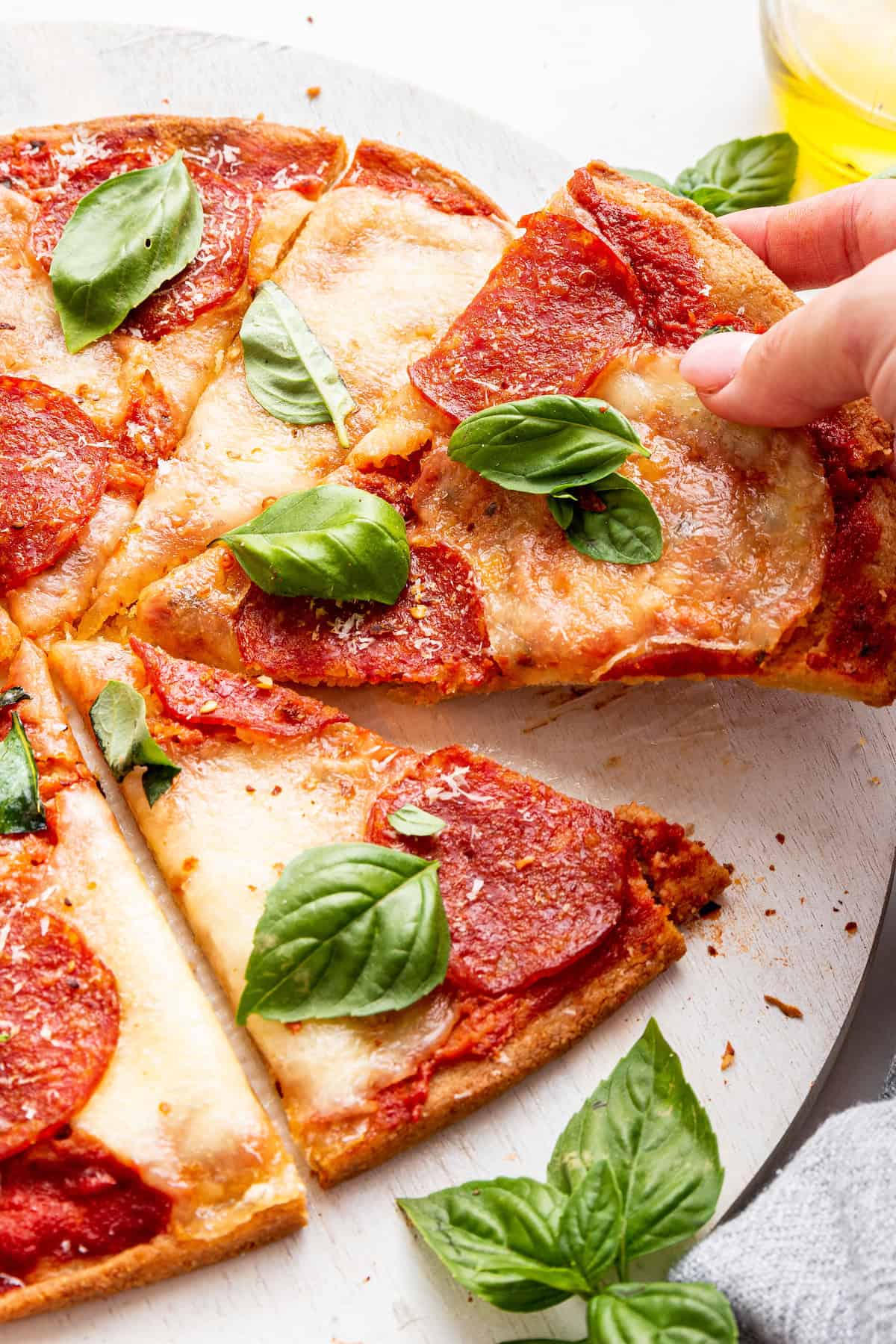 Hand pulling away slice of almond flour pizza with pepperoni