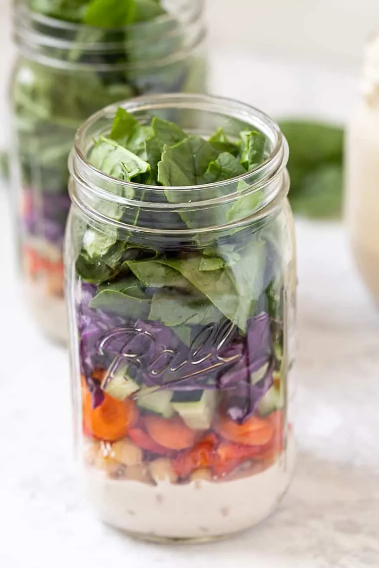 Side view of a mason jar salads with layers of rainbow veggies.