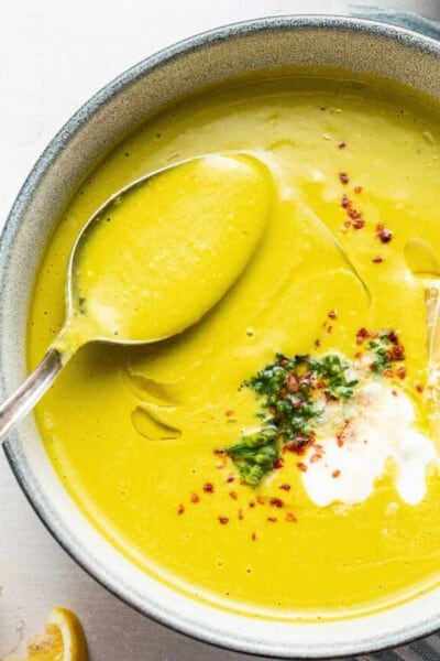 Close up overhead view of a bowl of broccoli soup topped with broccoli, chili flakes, and vegan creme fraiche, with a spoon taking a spoonful out