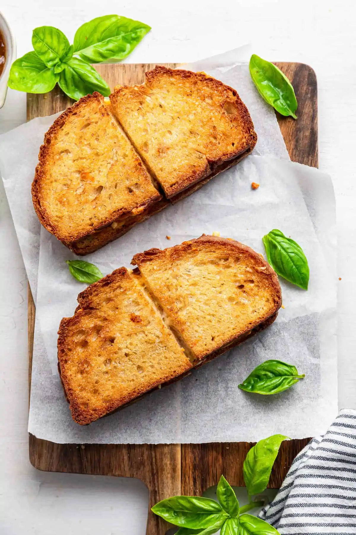 Two vegan air fryer grilled cheese sandwiches cut in half on a parchment-lined wooden cutting board.