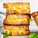 Vegan grilled cheese sandwiches stacked on top of one another, showing the melty cheese inside.