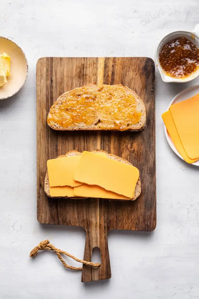 A grilled cheese sandwich is assembled on a wooden cutting board.