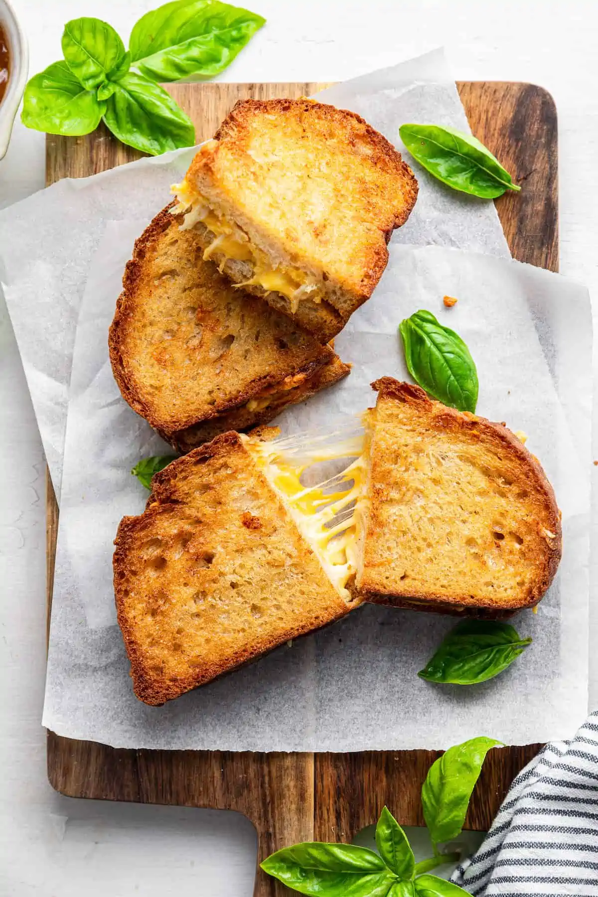 Two vegan air fryer grilled cheese sandwiches cut into halves on a parchment-lined wooden cutting board.