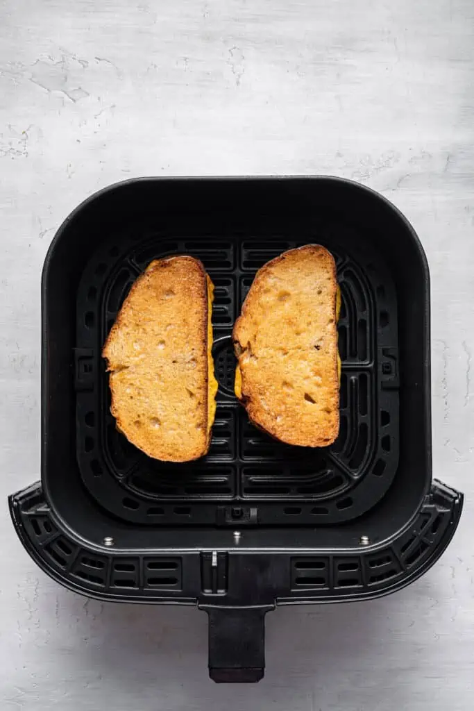 Two grilled cheese sandwiches inside the air fryer.