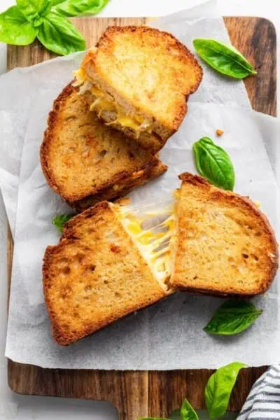 Two vegan air fryer grilled cheese sandwiches cut into halves on a parchment-lined wooden cutting board.