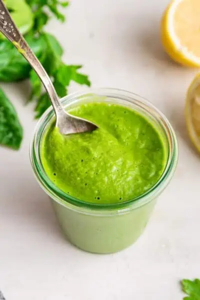 A spoon stuck into a glass filled with green goddess salad dressing.