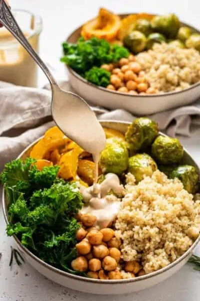 A spoon drizzles tahini dressing over an autumn harvest bowl.