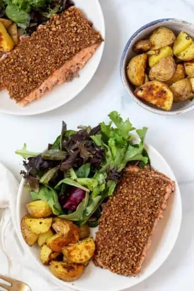 Pecan crusted salmon served on plates next to roasted potatoes and a side salad.