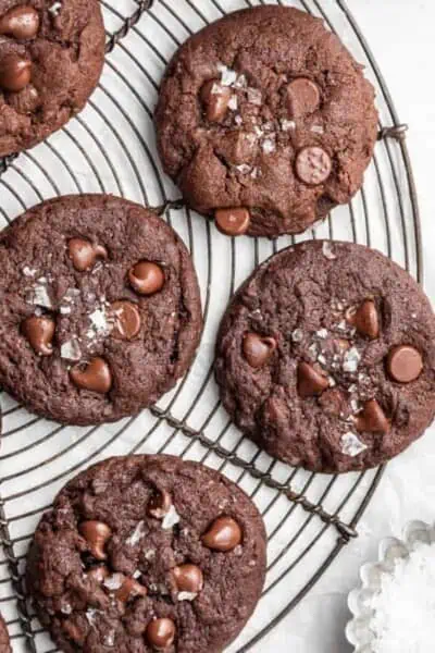 Four espresso cookies, topped with flaky salt, on a circular wire rack