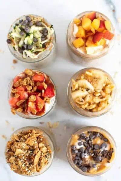 Overhead view of 6 different variations of overnight oats in glass jars.