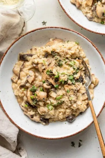 Two servings of vegan mushroom risotto on white plates.