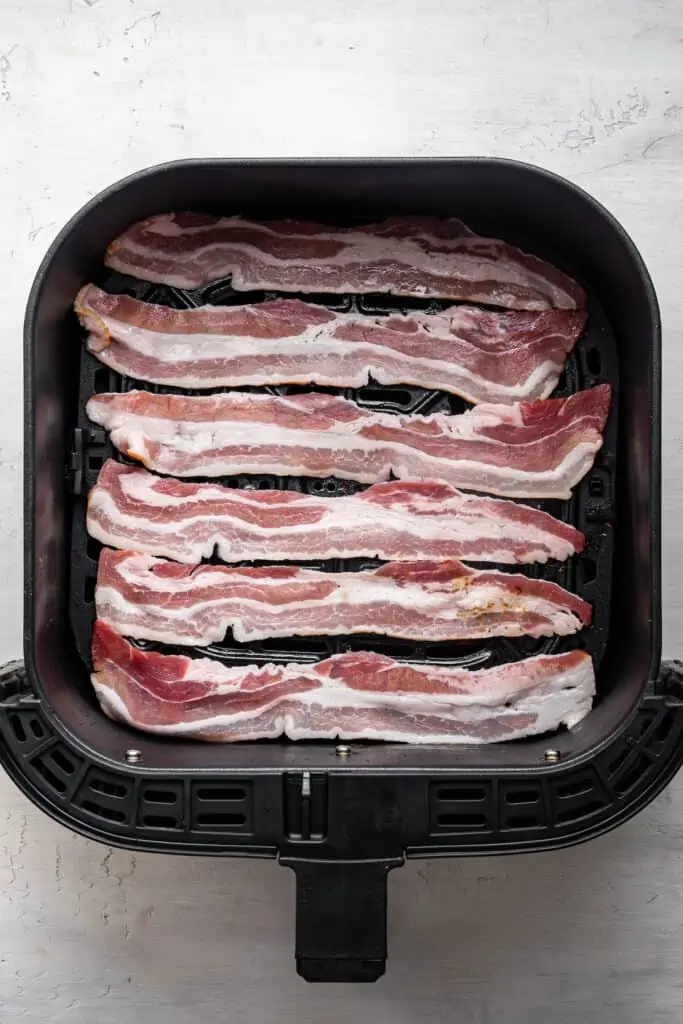 Uncooked bacon strips inside the air fryer basket.