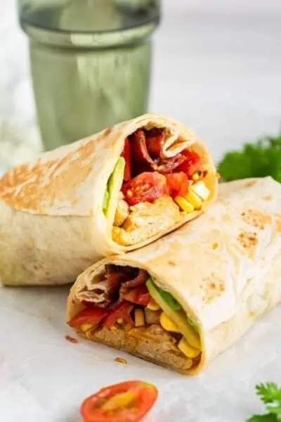 Two halves of a basic breakfast burrito filled with eggs, bacon, and veggies.