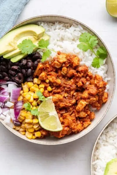 Vegan sofritas in a burrito bowl with rice, beans, avocado, veggies, and lime.