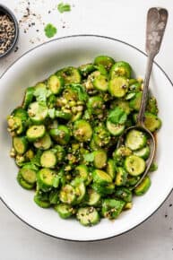 A serving bowl of cucumber salad with a serving spoon in it.