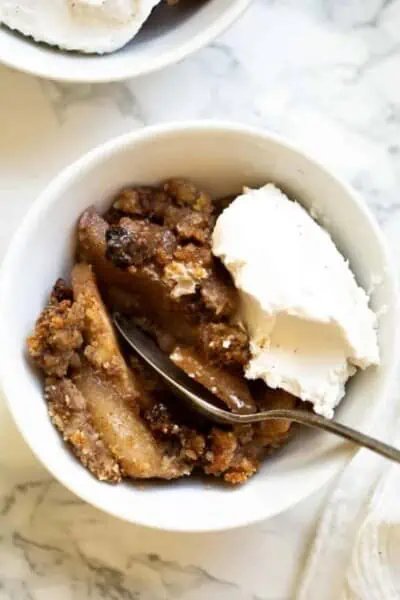 A serving of gluten-free apple crisp in a white bowl topped with vanilla ice cream.