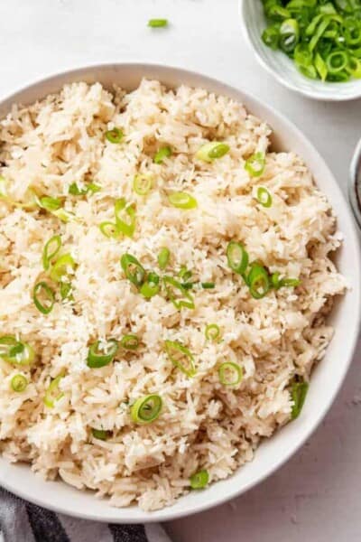 Overhead view of a serving bowl full of coconut rice topped with scallions, and a bowl of scallions.