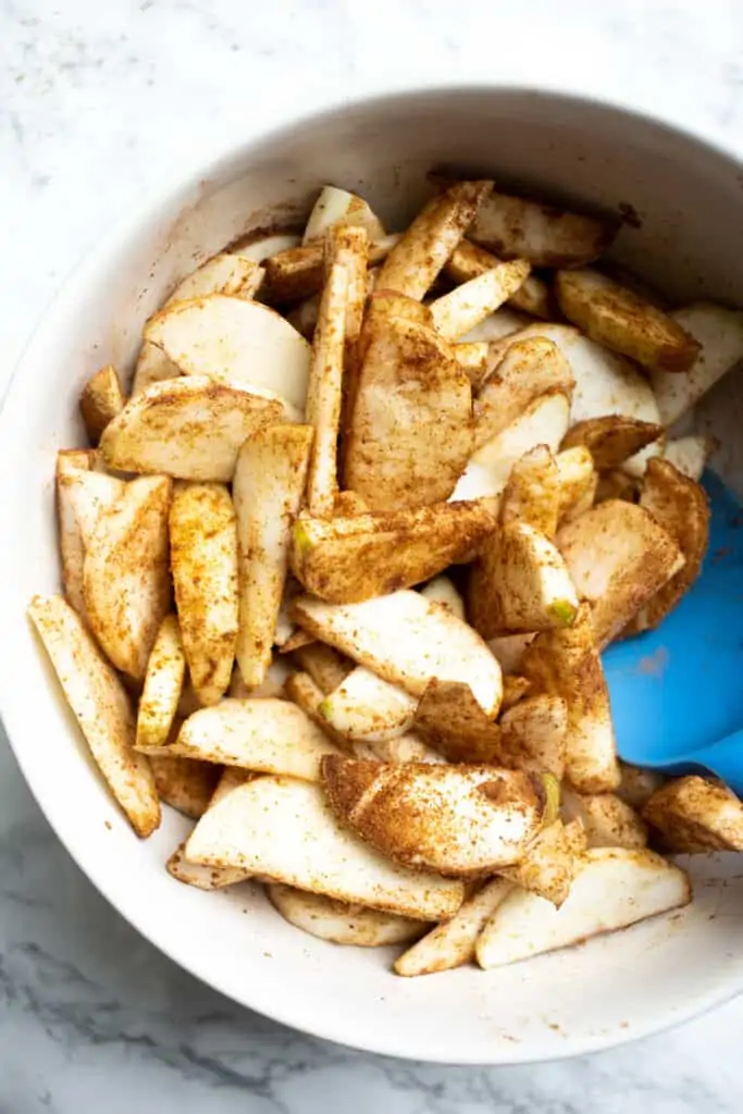 Apple slices stirred together with cinnamon sugar in a white bowl.