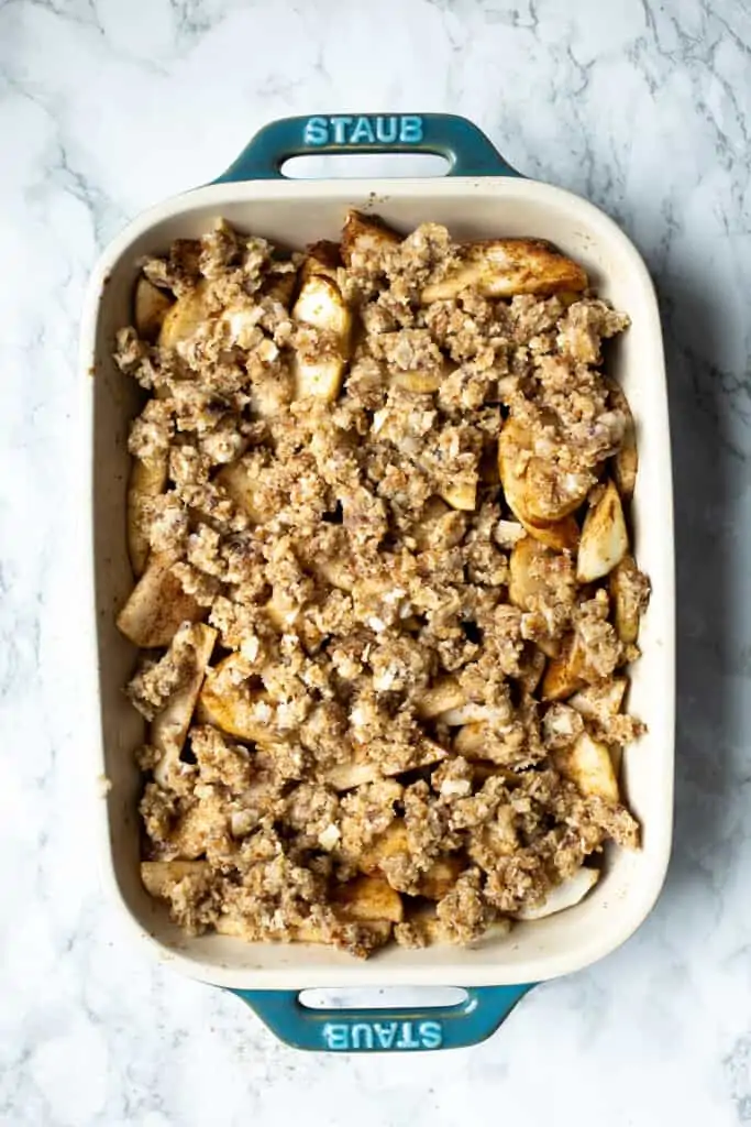 Cinnamon apples covered with gluten-free streusel topping in a white ceramic baking dish.