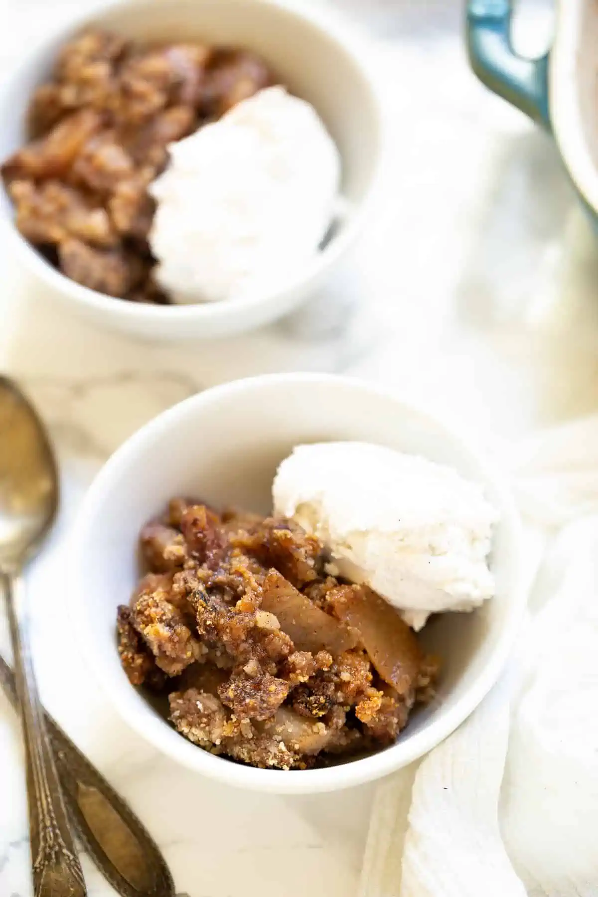 Two servings of gluten-free apple crisp in bowls, topped with vanilla ice cream.