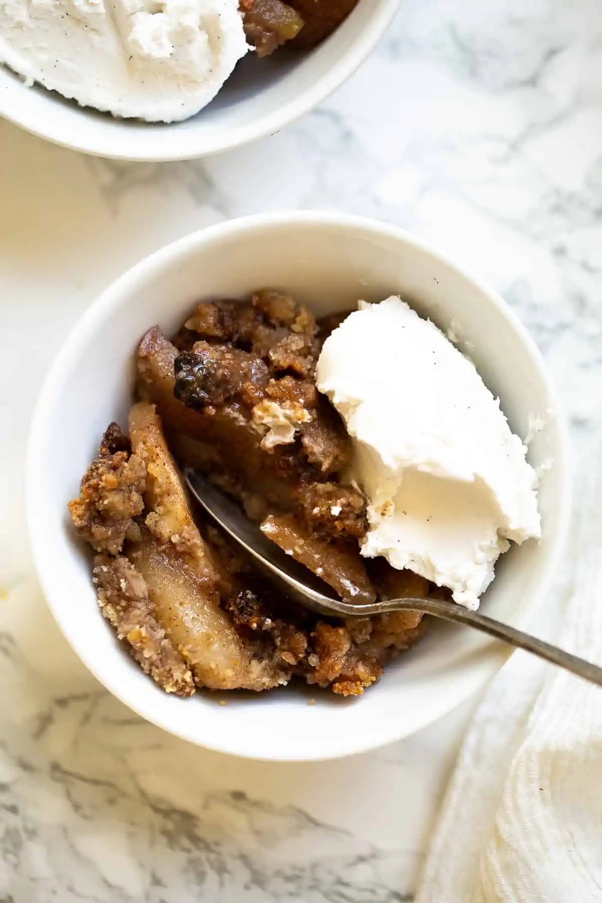 A serving of gluten-free apple crisp in a white bowl topped with vanilla ice cream.