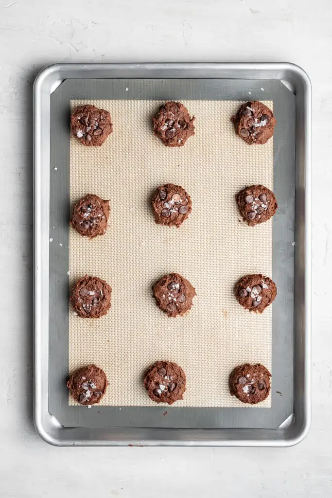 A baking sheet with a silpat on it, with 12 uncooked espresso cookies on it.
