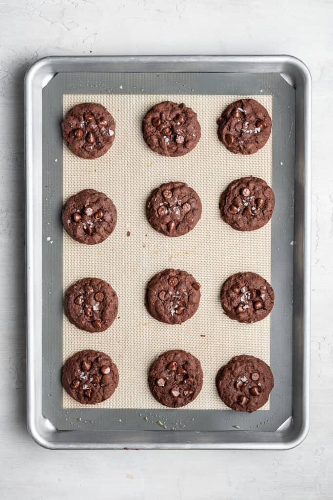 A baking sheet with a silpat and 12 fully cooked espresso cookies on it.