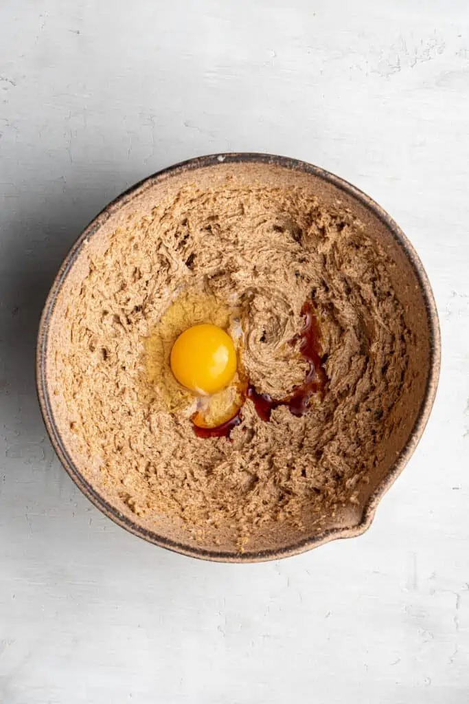 A mixing bowl of coconut sugar and vegan butter beaten together, with an egg and vanilla extract on top.
