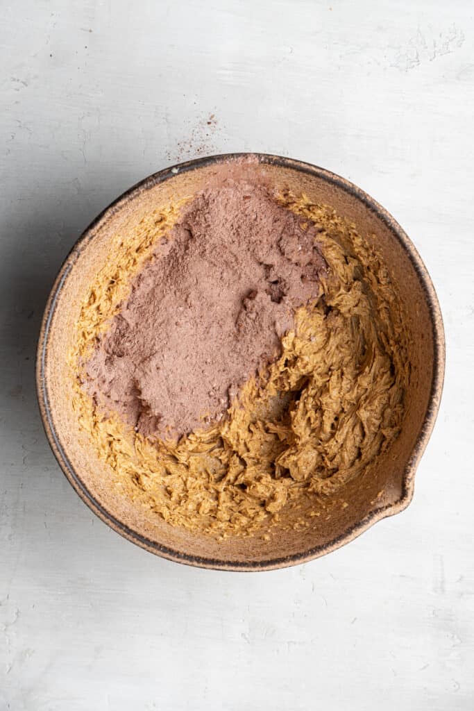 A mixing bowl filled with an egg, sugar, and vegan butter mixture, with some flour, cocoa powder, and espresso powder mixture on top.