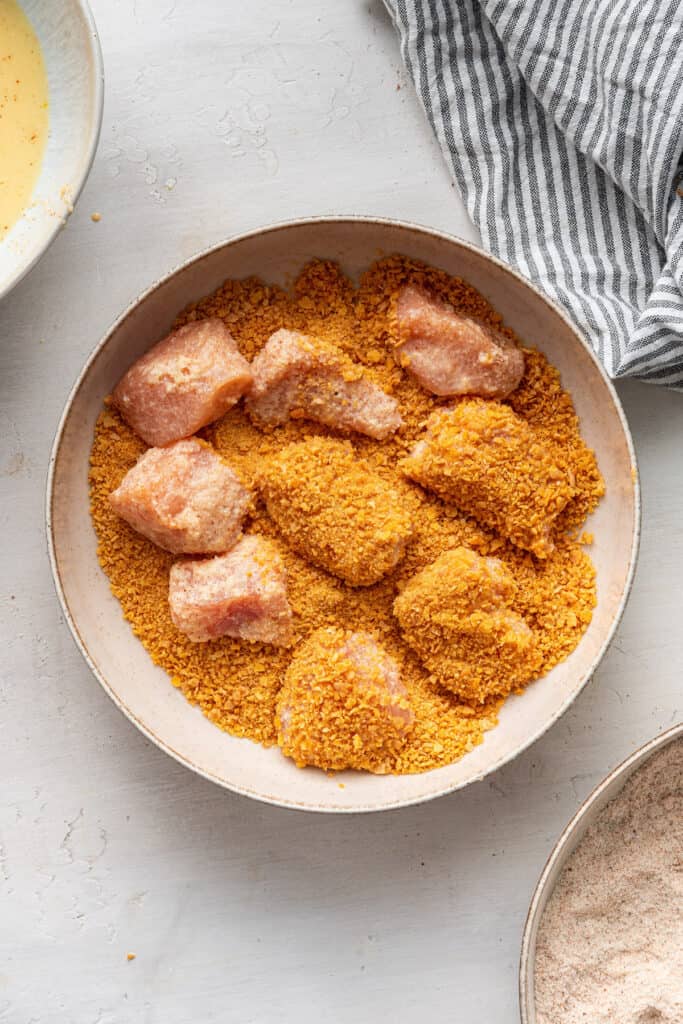 Chicken pieces being coated in breading.