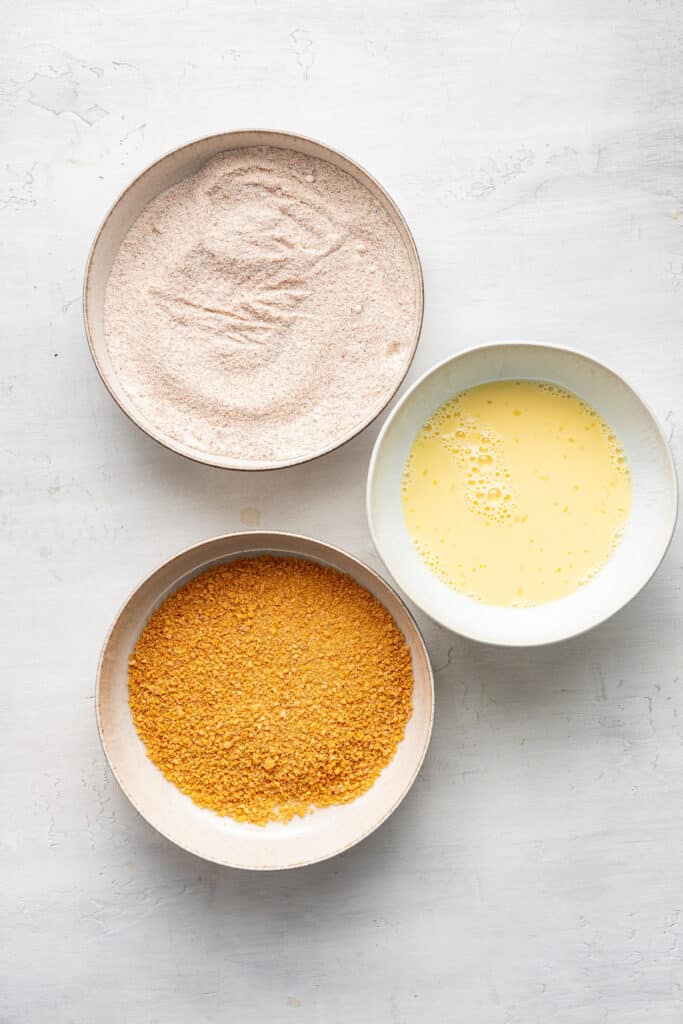 Three bowls filled with breading, egg and milk, and seasoning.