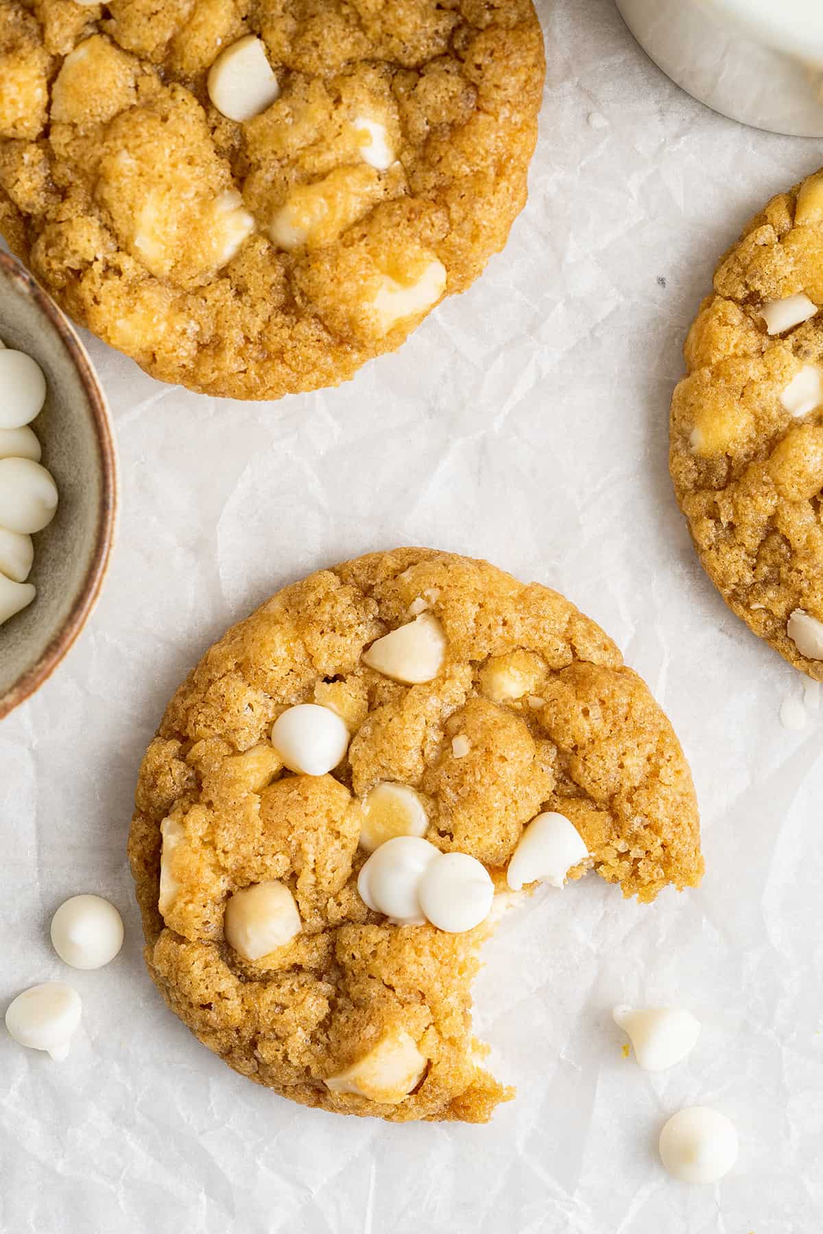 Overhead view of three cookies with white chocolate chips and macadamia nuts, with a bite taken out of one