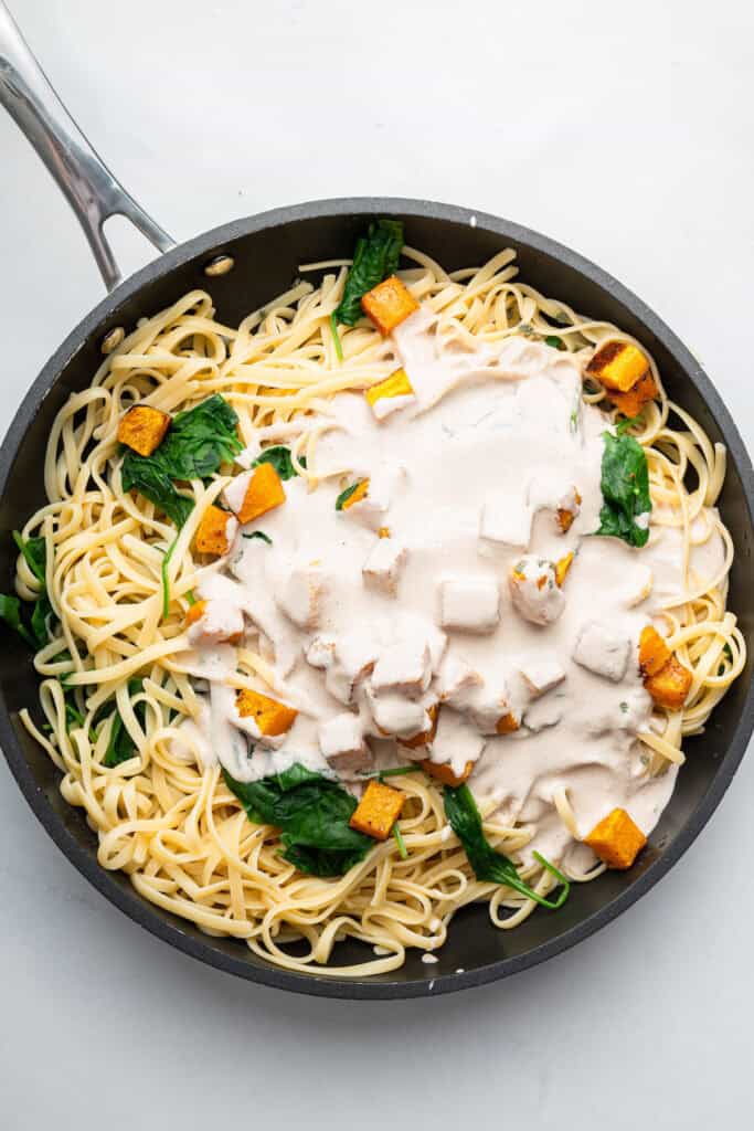 Creamy walnut sauce added to skillet of pasta