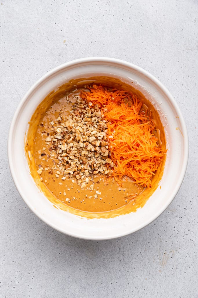 Overhead view of shredded carrots and nuts added to bowl of batter