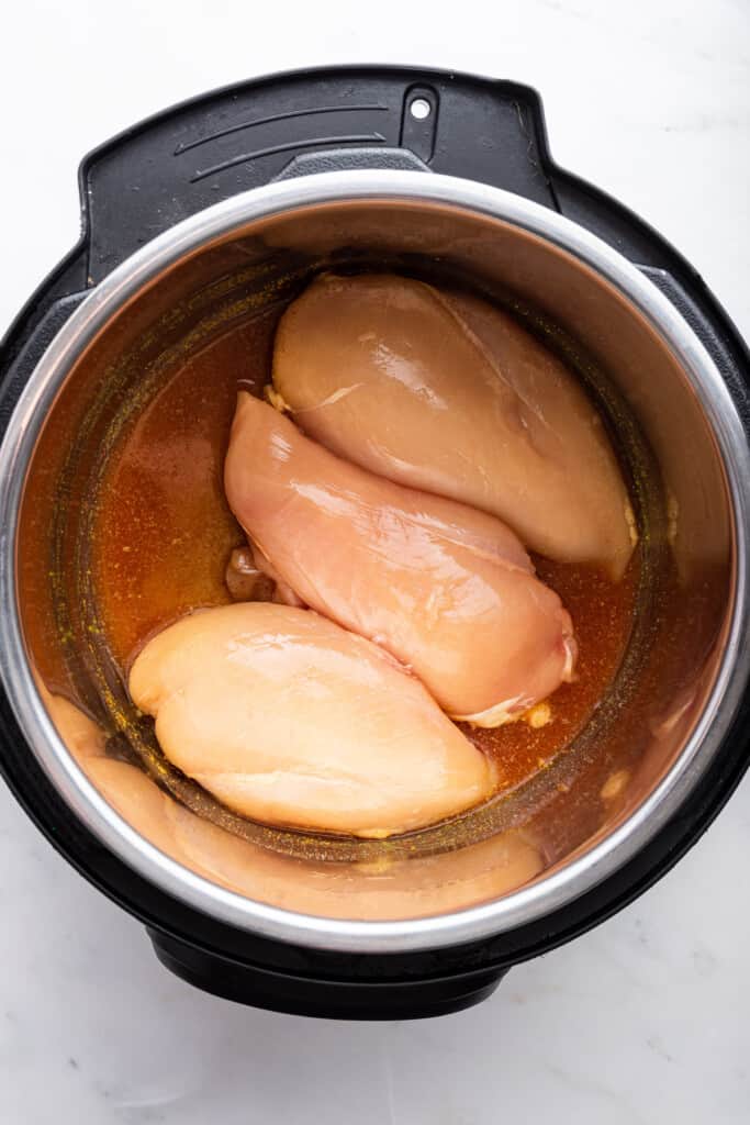 Overhead view of raw chicken breasts and broth in Instant Pot