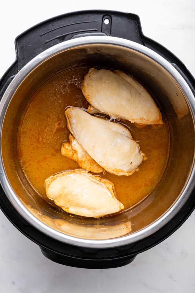 Overhead view of chicken breasts and broth in Instant Pot