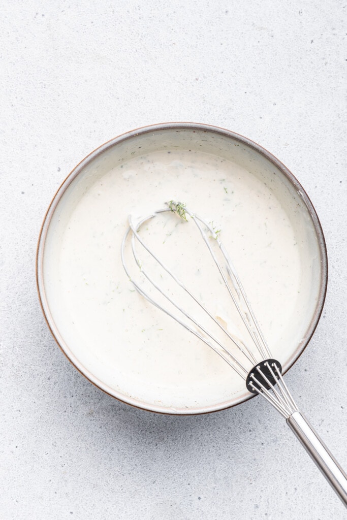 Overhead view of creamy surimi salad dressing in bowl with whisk