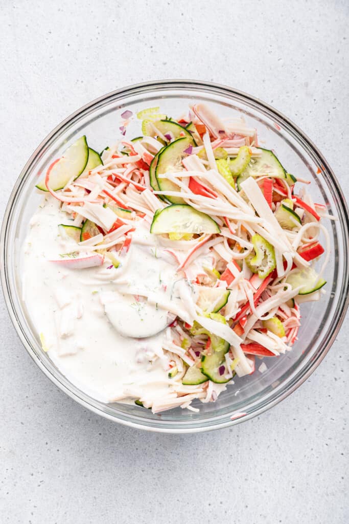 Overhead view of surimi salad ingredients and dressing in bowl before tossing